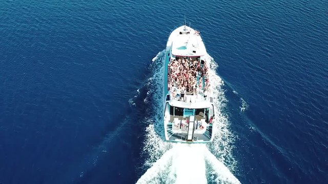 Top view of a speed boat sailing in the clear blue sea, people dancing on board the boat, party on a white yacht