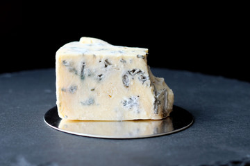 A piece of cheese with blue mold. Cheese Dorblu on a black board on a dark background.