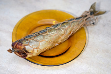 hot smoked mackerel on a glass plate. headless fish carcass in a smoking net. smoked fish top view.
