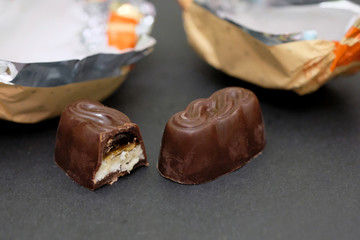 Chocolate candies on a black background. Bitten candy with jelly and bird milk. Stuffed chocolates and wrappers nearby.