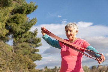 Caucasian older woman with sportswear and elastic band in the field doing sports