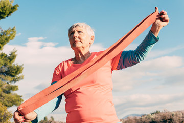 older woman with red t-shirt and elastic band practicing sport in the field
