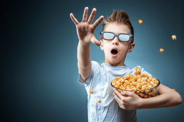 A boy holding popcorn in his hands watching a movie in 3D glasses, fear, blue background. The...