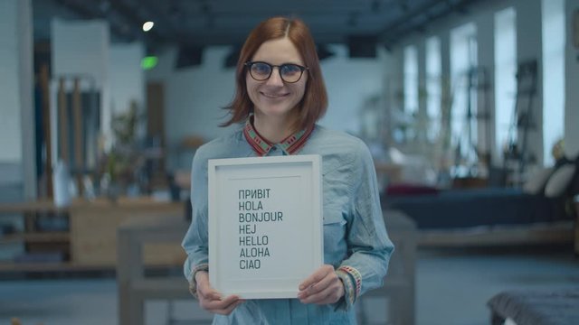 Young 30s brunette woman holding multilingual typescript welcoming text in white frame. Typewritten greeting text "Hello" in different languages