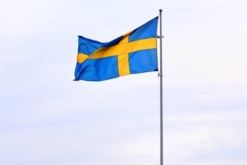 Sweden national flag on flagpole waving in the wind.  Blue-yellow flag of Sweden on blue sky background, selective focus. Stockholm state symbol. 