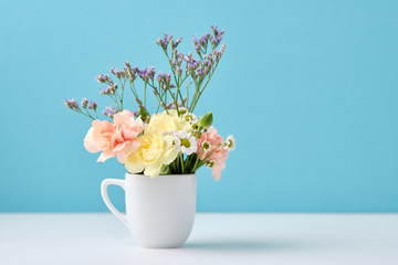 Beautiful little flowers bouquet in white mug on blue background