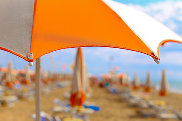 Bright multicolored orange white striped umbrellas with blue sunbeds on beautiful sand beach under blue sky. In front of adriatic sea. Summer holidays, vacation on the coast. Tourism in europe, Italy
