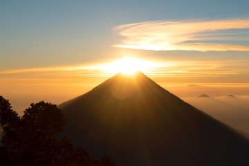 Sun shining above volcano crater, surrounded by smaller volcanoes in background
