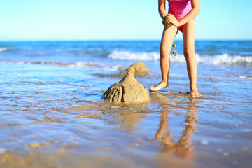 Legs of cute little girl spend holidays in pink one-piece swimsuit,builds sand castle,plays in the...