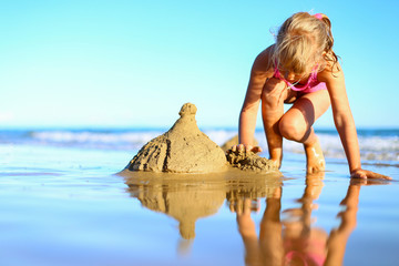 Cute little girl spend holidays in pink one-piece swimsuit, builds sand castle, plays in the water...
