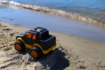 Children toy car jeep for little boys of black and yellow color on the sand near the water on the...