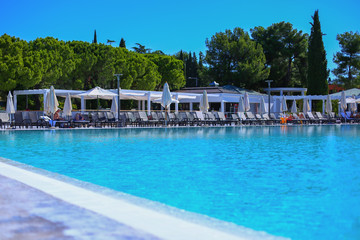 Swimming pool on outdoor zone of hotel.Umbrellas and sun protection tents for quests.Sunshine clear blue water with sunny reflections.Summer holidays and vacation.Tourism in Europe, Slovenia,Portoroz