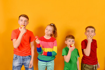 Four children eat an apple standing next to each other, guys on a yellow background in colorful color clothes.
