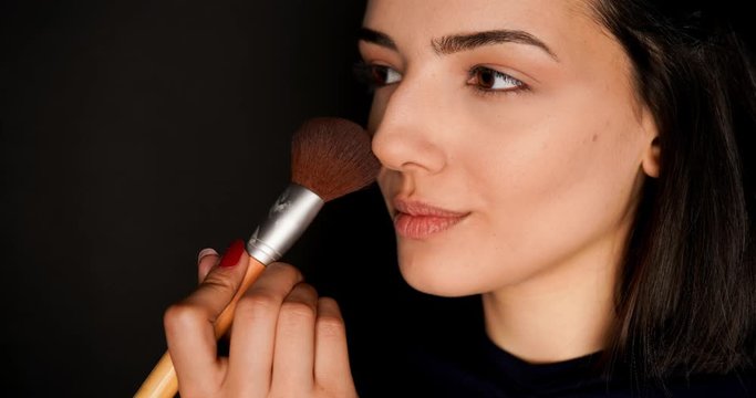 slow motion time lapse young woman applying blusher on her face using brush isolated on black background