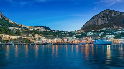 Fototapeta premium After sunset view of Marina Grande, Capri island, Italy. Illuminated streets of city are reflected in calm sea.