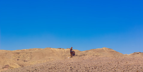 Fototapeta na wymiar lonely woman person in fluttering dress desert landscape panoramic scenic view dry warming nature outdoor environment of Israel sand stone ground and blue sky background empty copy space for your text