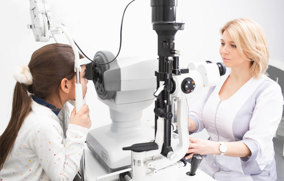 Female doctor looking very carefully at screen of ophthalmic tonometer to correctly check the girl’s vision. Vision correction