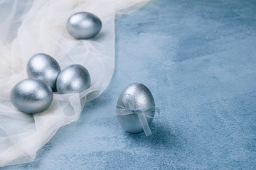 Silver grey painted Easter eggs on white napkin on textured blue background. Happy Easter greeting...