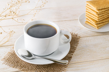 Hot coffee in white elegant cup and stack of sweet square cookies on a white wooden table. Steaming hot morning beverage and pastries.