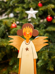 Handgearbeiteter Engel vor einem Weihnachtsbaum