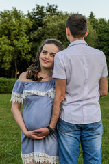 Obraz premium A young family in love in which the husband hugs a pregnant wife in the park