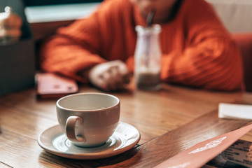 Girl teenager sitting in cafe at a table in red knitted sweater waiting and looking typing in phone messages. Milk chocolate cocktail in a glass reusable bottle with a foil cap and a disposable tube