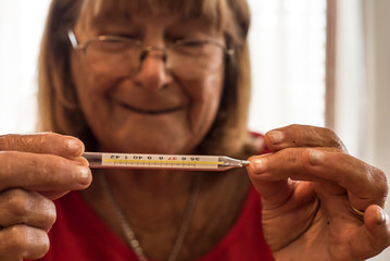 older woman measuring her temperature with the thermometer