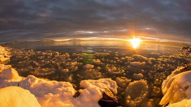 Sunset timelapse over Utah Lake as sky lights up viewing ice in water along snow covered shoreline.