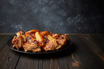 Fried potatoes with meat, on a black plate, on a black background