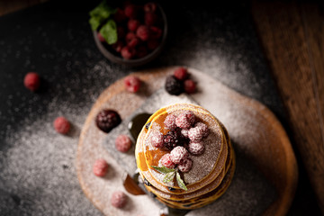 Pancakes with raspberries, blackcurrants, caramel sauce and sugar powder on the dark background. American cuisine. Dessert. Copy space. Place for text. Preparing breakfast. Place for recipes. Top view