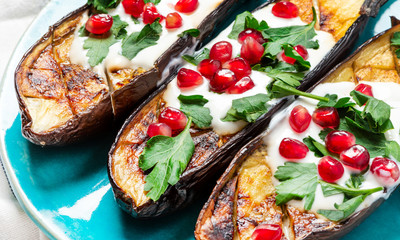Grilled eggplant with yogurt, parsley, garlic and pomegranate on a blue ceramic plate, closeup....