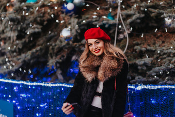Beautiful young girl in festive scenery. The girl smiles slightly. Behind the girl is a Christmas tree with bubbles and lights. Cute girl doing herself selfie