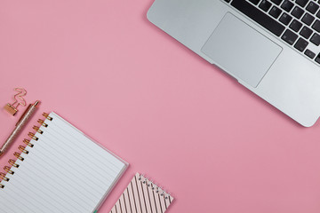 Modern female working space, top view. Laptop, notebooks, pen in rose gold color, clamp on pink backround, copy space, flat lay. Desktop of blogger, freelancer. Work from home concept. Horizontal