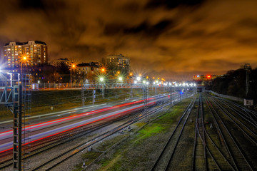 The blurred red line of lights from a train rushing into the distance along the railway tracks at night in the city.