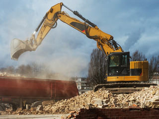 An excavator breaks down an old building. Dust, bricks and broken walls.