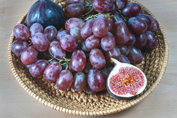 red grapes and fresh fig fruits in a straw basket on a light wooden background
