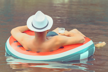 a man in a white hat lies on an air mattress in the water. summer holiday concept