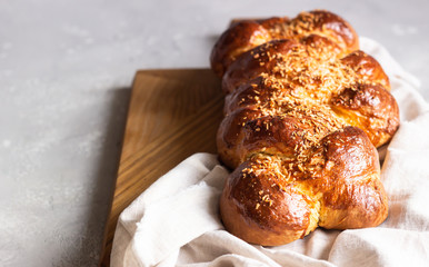 Homemade challah bread on a wooden cutting board over light grey stone background. Shabbat, hebraism traditional bread.