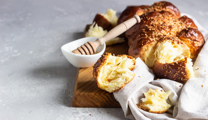 Homemade challah bread on a wooden cutting board over light grey stone background. Shabbat, hebraism traditional bread.