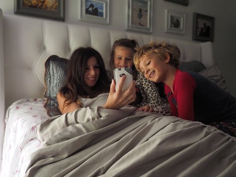 Female taking a selfie with the kids while lying on the bed