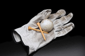 Golf Still Life. A used golf glove with tees and a dirty golf ball on black with copy space.