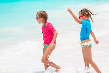 Naklejka premium Little happy funny girls have a lot of fun at tropical beach playing together. Sunny day with rain in the sea