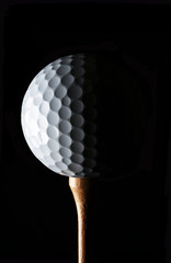 Golf Still Life. Closeup low key golf ball on wood tee with strong side light, against a black background.