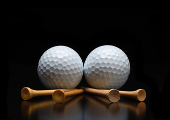 Two golf balls with tees laying on a black reflective surface. Low angle with copy space.