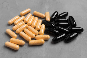 Two piles of black and yellow capsule pills on gray background, top view.
