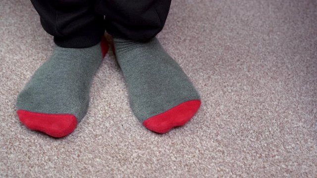 Feet in red-grey socks on a light brown carpet rub against each other