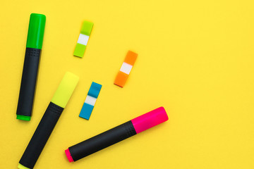 Multicolored markers and stickers on a yellow background, top view, copy space