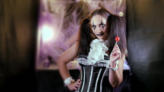 Portrait of a woman. A clown with a smile in corset with a white collar on the neck. Model with makeup for Halloween. Woman flirting. The girl with the red Lollipop.