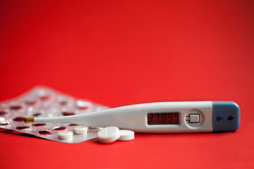 blister with tablets and a thermometer on a red background