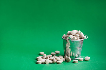 Fototapeta na wymiar A bucket full of pills scattered on a green background.